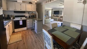 A compact kitchen with white cabinets, a microwave, a stove, and a dining area with a table and chairs. - Lake house retreat (Abbeville)
