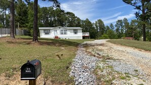 A mailbox in a rural setting with a gravel path leading to a white house surrounded by trees. - Lake house retreat (Abbeville)