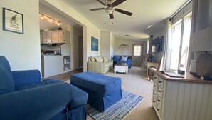 A spacious living room with a blue sofa set, a ceiling fan, and a kitchen in the background. - Lake house retreat (Abbeville)