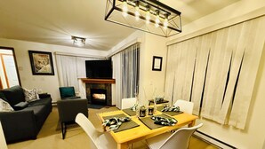 Una sala de estar con chimenea, una mesa de comedor preparada para cuatro personas y un sofá.