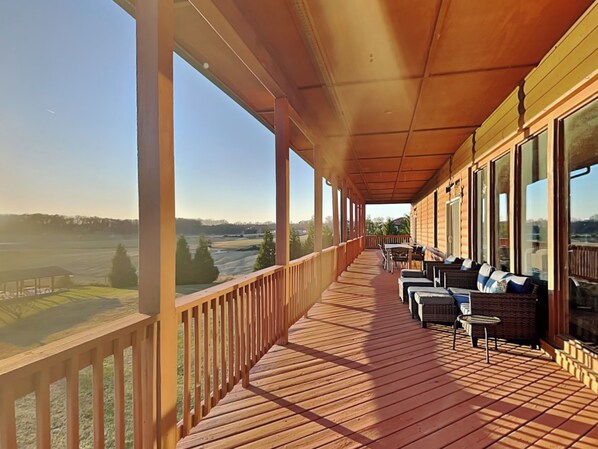 A covered wooden deck with outdoor seating and large windows offering a view of a rural landscape. - Wonderland Cove by Jackson Mountain Rentals (Dandridge)