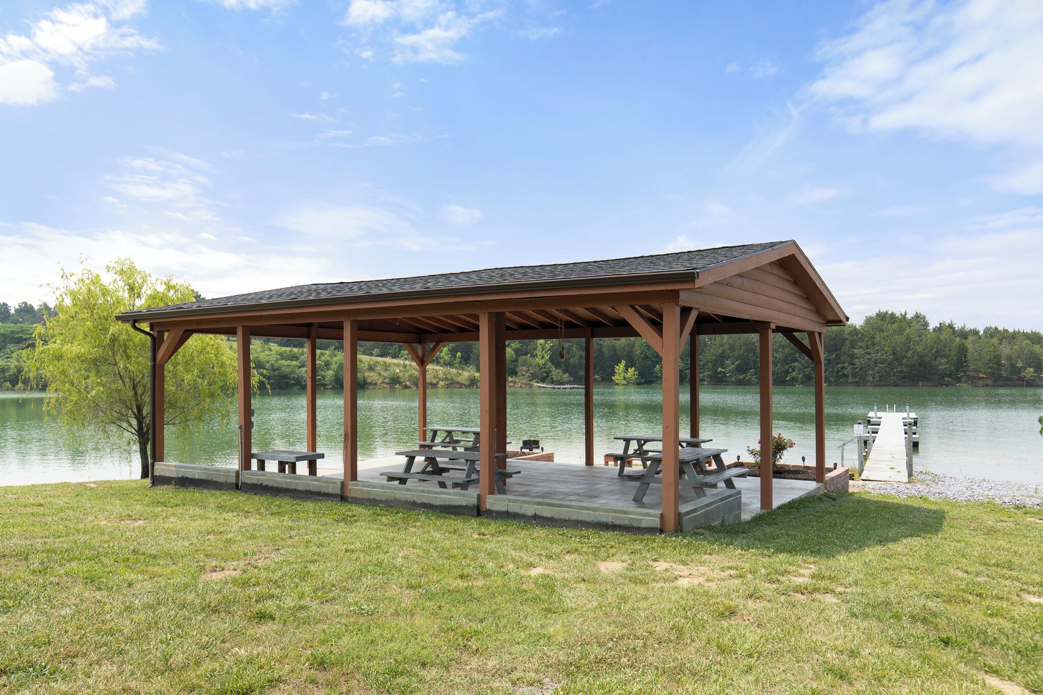 Un área de picnic techada con bancos y mesas junto a un lago.