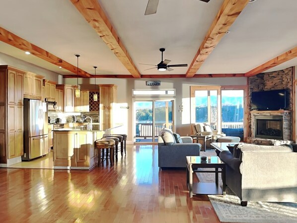 A spacious living area with a kitchen, wooden beams, a fireplace, and a balcony with a view. - Wonderland Cove by Jackson Mountain Rentals (Dandridge)
