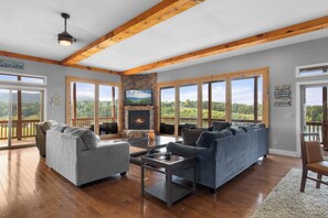 A spacious living room with a stone fireplace, large windows, and a view of the outdoors. - Wonderland Cove by Jackson Mountain Rentals (Dandridge)
