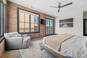 Une chambre à coucher avec un grand lit, un canapé, un ventilateur de plafond et une vue sur l’extérieur grâce à de grandes fenêtres.