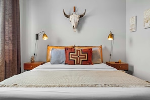 Une chambre à coucher avec un grand lit, deux tables de chevet, un crâne fixé au mur et deux lampes murales.