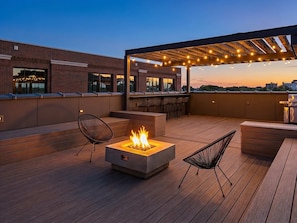 Une terrasse sur le toit avec un foyer, des sièges et des guirlandes lumineuses.