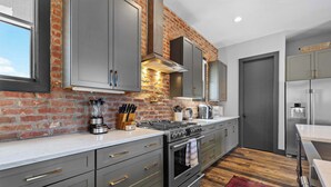 A modern kitchen with grey cabinets, a brick wall, a gas stove, and a stainless steel refrigerator. - 2 Luxe Nashville Homes | Near to Broadway (Nashville)