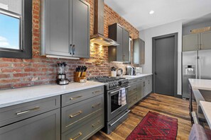 A modern kitchen with grey cabinets, a brick wall, a gas stove, and a stainless steel refrigerator. - 2 Luxe Nashville Homes | Near to Broadway (Nashville)