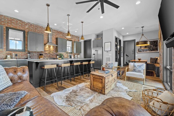 A modern kitchen with a brick wall, bar stools, and a dining area with a table and chairs.