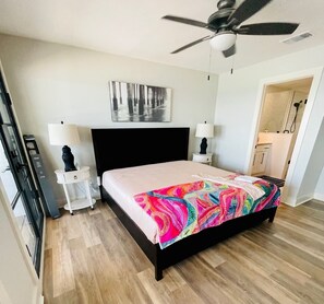 Une chambre moderne avec un grand lit, deux tables de chevet, un ventilateur de plafond et une vue sur la salle de bain.