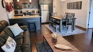 Een moderne keuken met donkere kastjes, een roestvrijstalen koelkast en een centraal eiland. Er is een zithoek met een houten tafel en stoelen.
