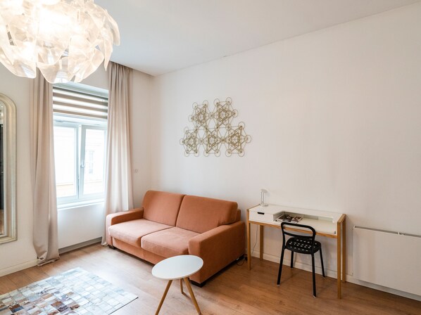 Una sala de estar moderna con un sofá, una mesita redonda, un escritorio con una silla y un adorno de pared.