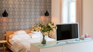 A bedroom with a bed, a TV on a dresser, and a vase with flowers. - Baross Boutique Apartman Urban Rooms (Gyor)