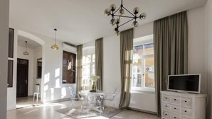 A spacious living room with a dining area, a TV stand, and large windows with curtains. - Baross Boutique Apartman Urban Rooms (Gyor)