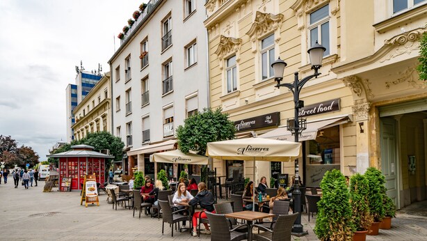 An outdoor cafe area with tables and chairs, surrounded by buildings with ornate facades and outdoor seating. - Baross Boutique Apartman Urban Rooms (Gyor)