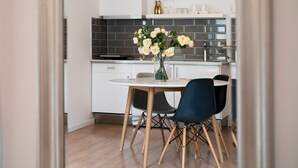 A modern kitchen with white cabinets, a black tiled backsplash, and a dining area with a round table and two chairs. - Baross Boutique Apartman Urban Rooms (Gyor)