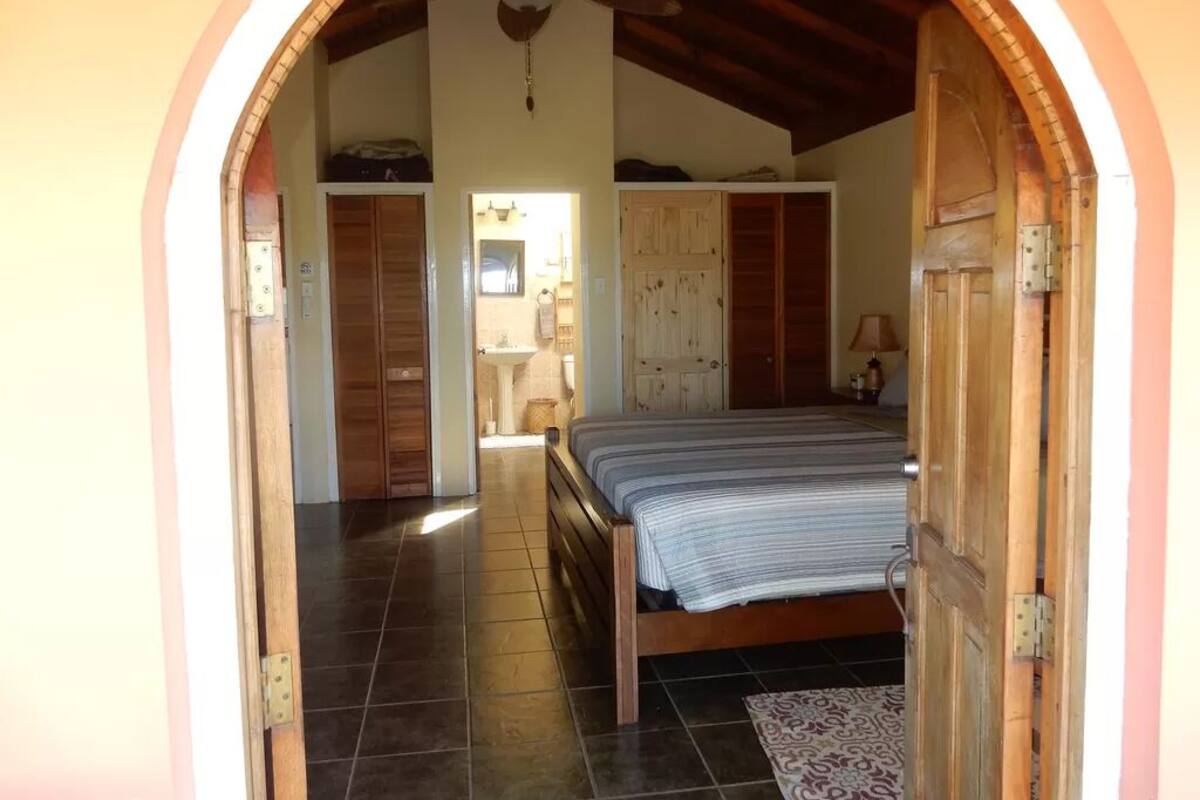 A bedroom with a bed, wooden wardrobe, and a bathroom visible through an archway.