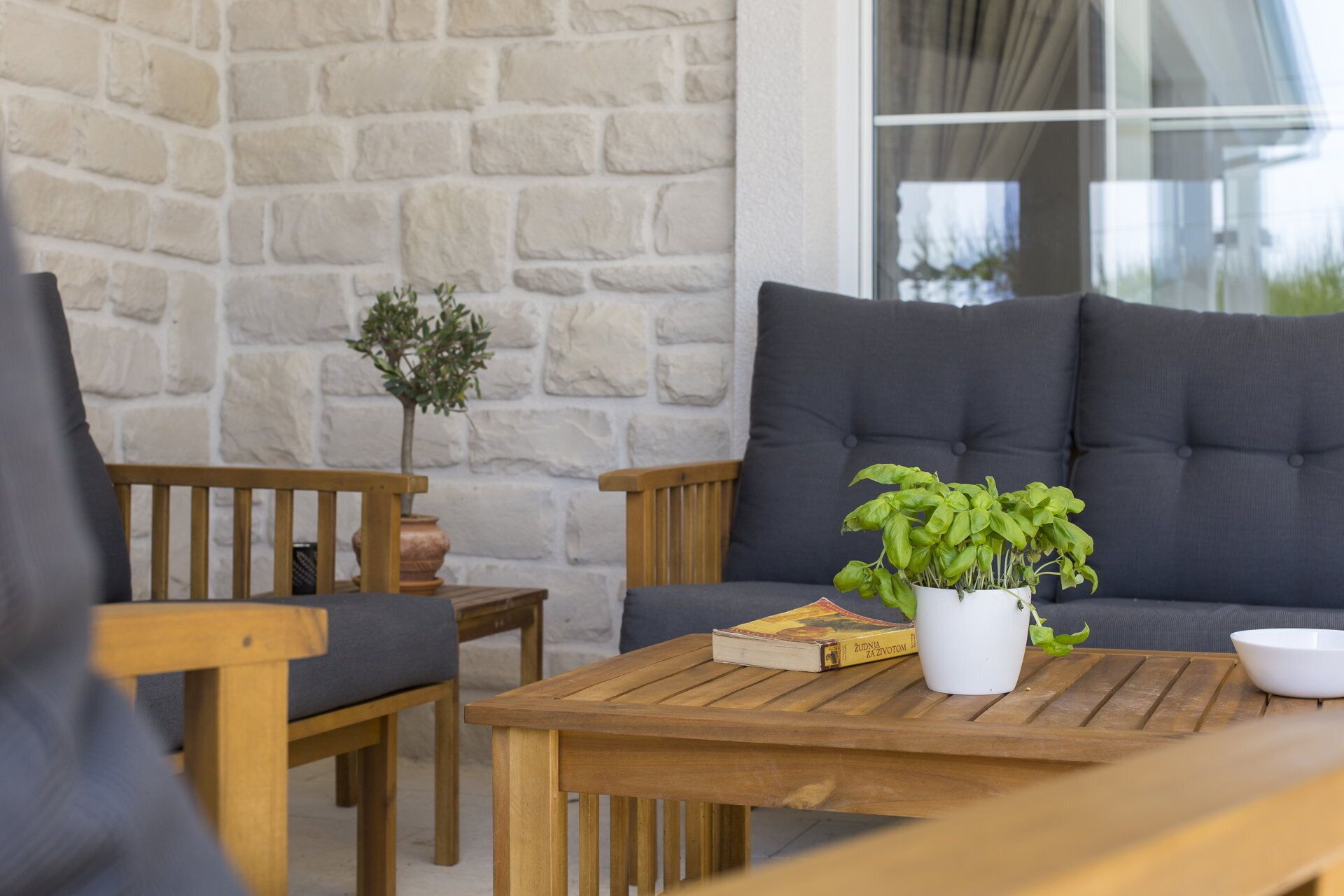 Een houten tafel met een boek en een plant in pot, een grijze bank en een bijzettafeltje met een bloevas.