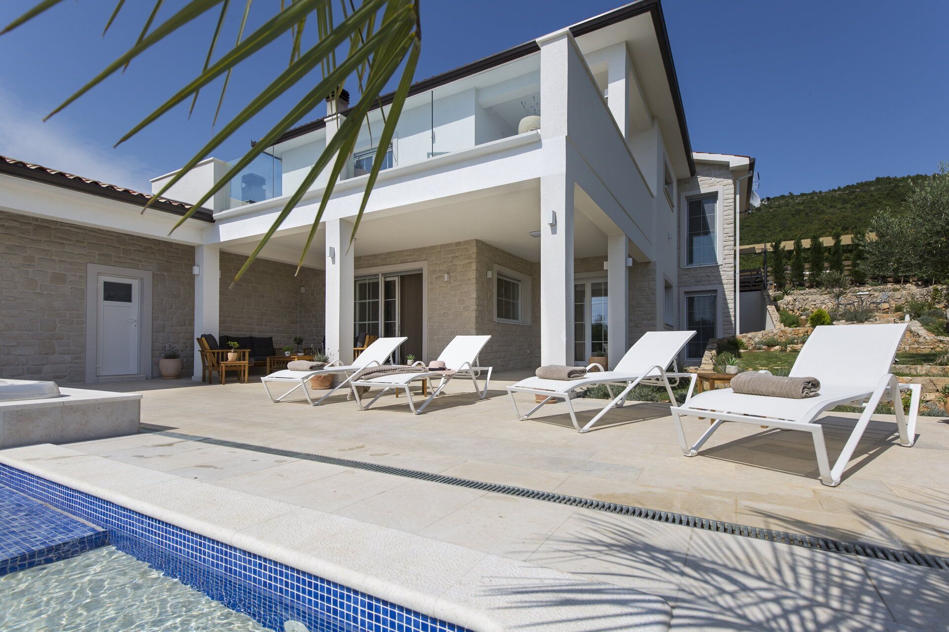A modern villa with a pool, sun loungers, and a stone facade.