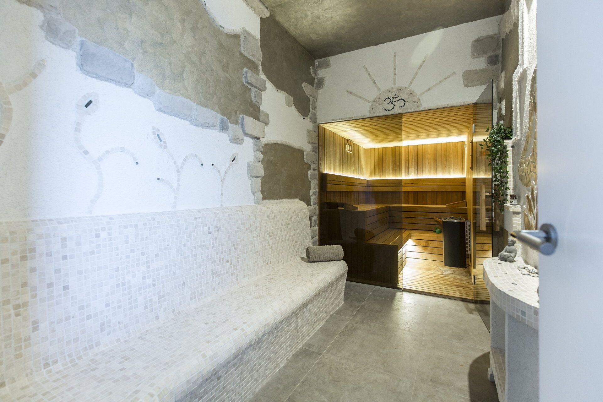 A spa room with a wooden bench, a stone wall, and a wooden ceiling with a sun design.