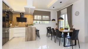 A modern kitchen with a central island, dining area with chairs, and a large window with curtains. - Villa Sunny Day with Pool (Labin)