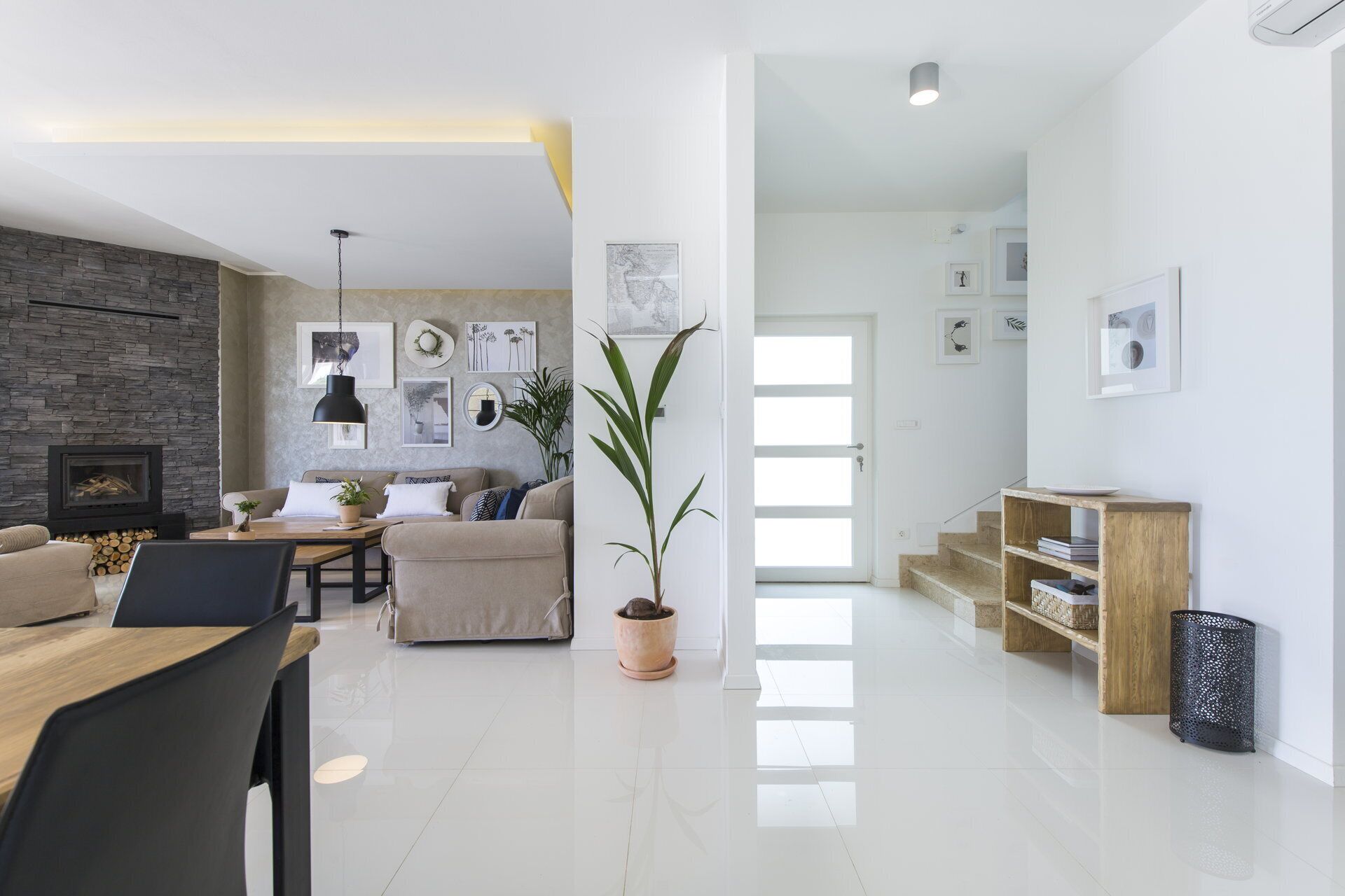 A modern living room with a stone fireplace, a sofa, a dining table, and a staircase leading to another level.