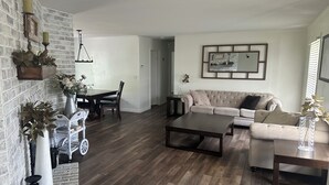 Ein Wohnzimmer mit Holzboden, einer Couch, einem Couchtisch und einem Essbereich mit Tisch und Stühlen.