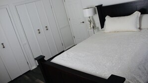 Ein Schlafzimmer mit Bett, weißen Wänden, einem dunklen Holz-Kopfteil und einem Nachttisch mit Lampe.