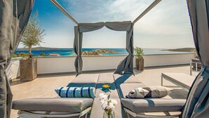 Un espacio de estar al aire libre con luz solar, vistas al mar y una isla distante.