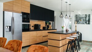 Cocina moderna con armarios de madera, refrigerador de acero inoxidable, cafetera y barra con taburetes.