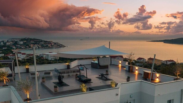A rooftop terrace with outdoor seating, a covered area, and a view of the sea and town.