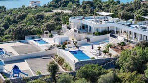 A modern resort with multiple swimming pools, a large outdoor deck, and a view of the surrounding hills and water.