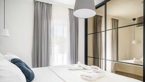 A modern hotel room with a large bed, white linens, and a view through a glass partition.