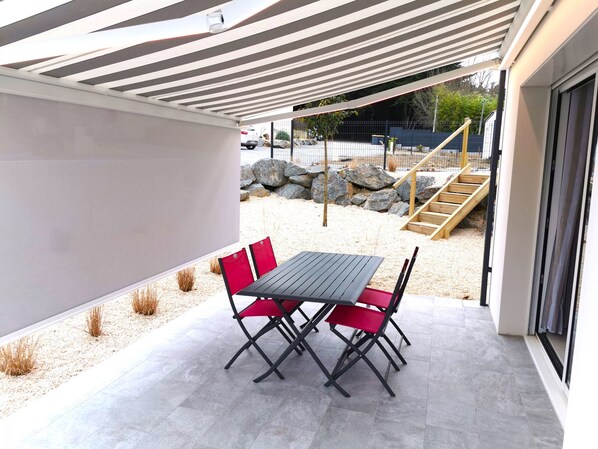 A covered patio with a table and chairs, a stone wall, and a view of the street.