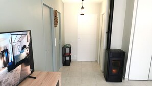 Una sala de estar moderna con un televisor, una mesa de madera, un calentador negro y un pasillo que conduce a una puerta.