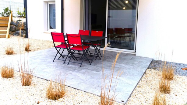 Un patio exterior con mesa y sillas, un ventanal corredero y suelo de grava.