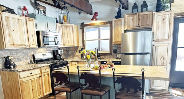 Enjoy cooking in this well-equipped kitchen with a central island and bar stools, featuring a refrigerator, oven, and microwave.