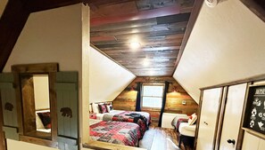 Cozy attic bedroom with two beds, a window with a view, and a door featuring a bear silhouette.