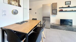Eine moderne Küche mit Kühlschrank, einem Esstisch mit Stühlen, einem Flachbildfernseher und Dekorationen auf Regalen.