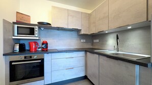 Eine moderne Küche mit Mikrowelle, Kaffeemaschine und Wasserkocher auf der Arbeitsfläche, einem Spülbecken mit Armatur und einem Herd.