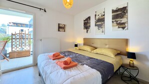 Ein Schlafzimmer mit einem Bett, zwei Kissen, einem Nachttisch, einer Lampe, einem Wandbild und einem Balkon mit einem Stuhl.