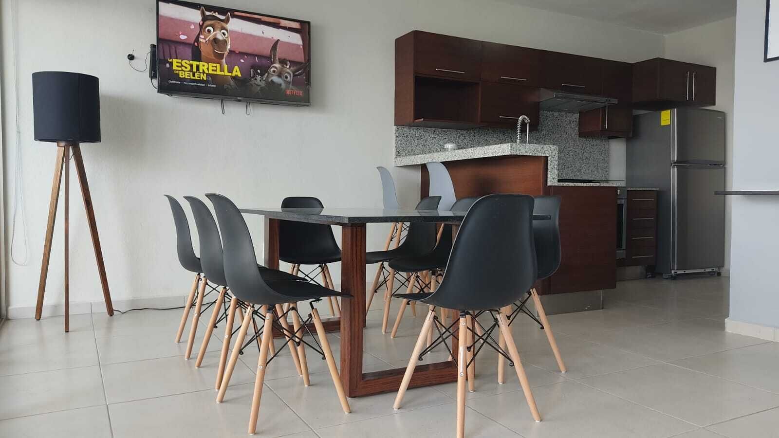 Una cucina moderna con mobili in legno scuro, un frigorifero in acciaio inossidabile e un'area pranzo con un tavolo in vetro e sedie nere.