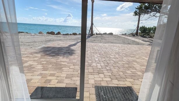 On aperçoit, à travers une porte vitrée, un patio dallé avec une grille métallique, un plafond en bois et un ciel dégagé.