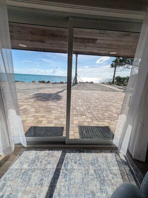 A view through a glass door to a paved patio with a metal grate, a wooden ceiling, and a clear sky. - Newly Remodeled-Beachfront Home with Pool/Spa! Private Island Living on 1 Acre (Englewood)