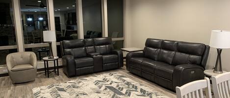 A modern living room with a leather sectional sofa, a small armchair, a dining table, and a patterned rug.
