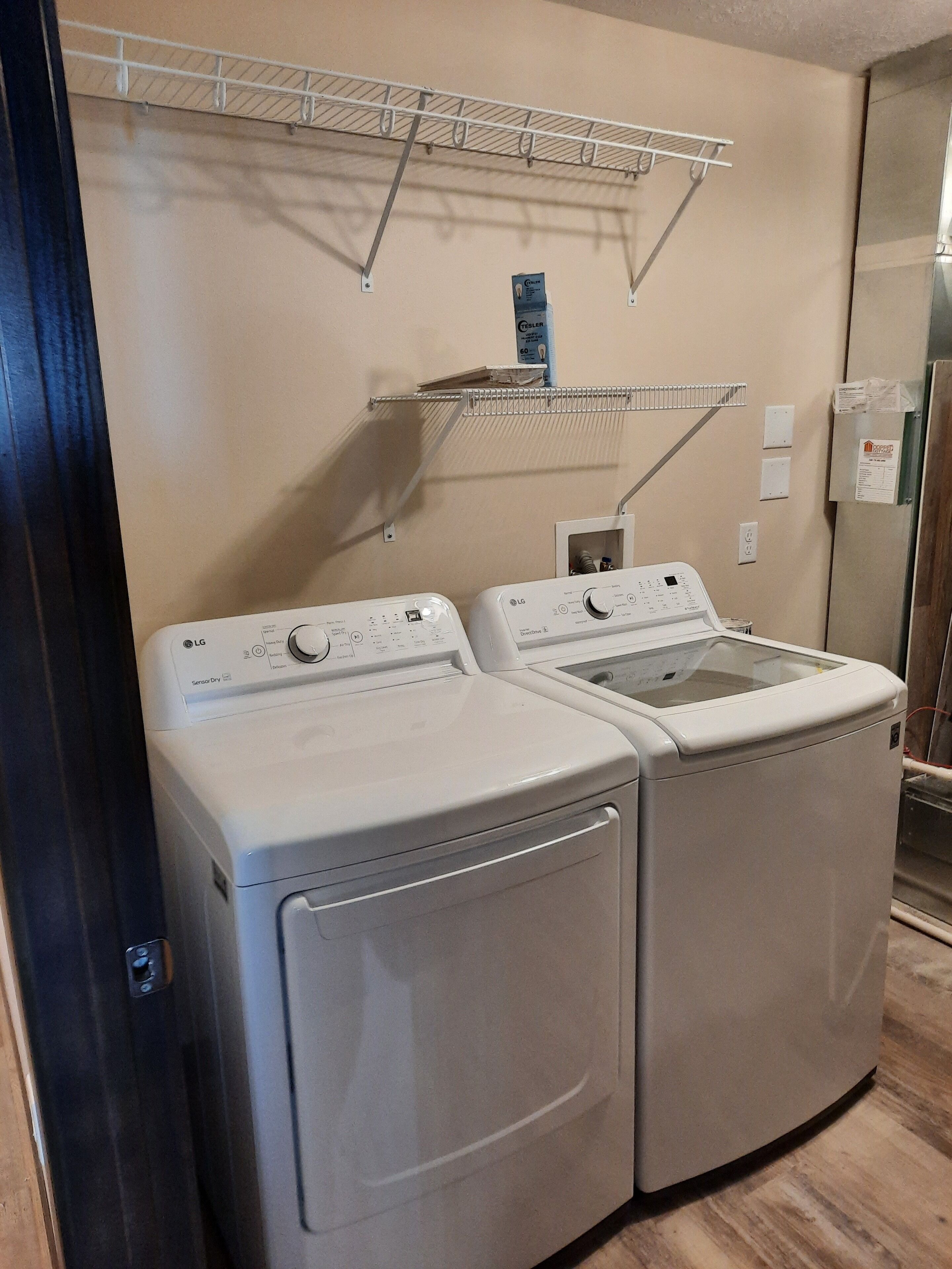 A laundry area with two front-loading washers and dryers, a metal drying rack, and a wall-mounted electrical box.