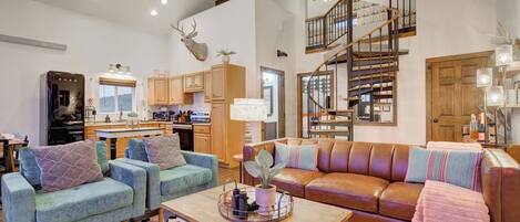 A spacious living room with a sofa, armchairs, a coffee table, and a staircase leading to an upper level.