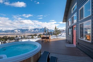 A hot tub on a wooden deck with a mountain view, a dining area, and a building with large windows. - Sky Cabin • Mountain Sauna • Hot Tub • Yellowstone (Emigrant)