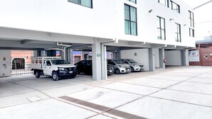 A parking garage with multiple levels, a white building with large windows, and a truck parked in the foreground. - Villas Analco Apartments (Puebla)